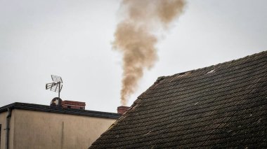 Isınma sırasında bir apartmanın bacasından siyah duman yükseliyor ve çatıyı ısıtıyor. Kışlık sobanın dumanı. Şehirlerdeki hava kirliliği.
