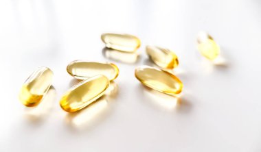 Kaşık içinde altın sarısı haplar beyaz arka plana saçılmış. Besin takviyelerinin yumuşak kapsülü balık yağı omega 3 vitamini D3 vitamin E vitamini kapsülleri beyaz arka planda