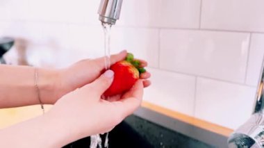 Kadınların elleri mutfakta musluk suyu ile kırmızı çilekleri iyice yıkar. Çilek mevsimi. Yüksek kalite 4k görüntü