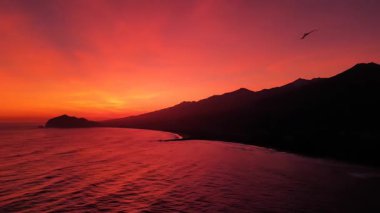 Okyanusun altında hafif bir hareketle dalgalanır, erimiş kıpkırmızı tonlarda, yukarıdaki ateşli gradyanı yansıtır.