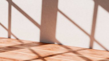 Minimalist duvar ve ahşap zemin sıcak güneş ışığıyla aydınlatılarak kalın geometrik pencere gölgeleri oluşturuldu. Tasarım modelleri ve markalaşma görselleri için mükemmel..