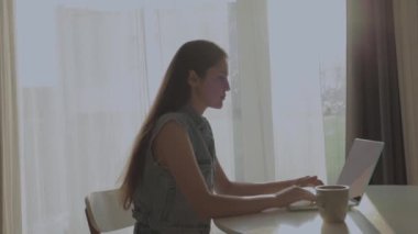 Neşeli, mutlu, pozitif ve güzel bir iş kadınının evde oturup bilgisayarını kullanması video konuşması ve mutfakta el sallaması..