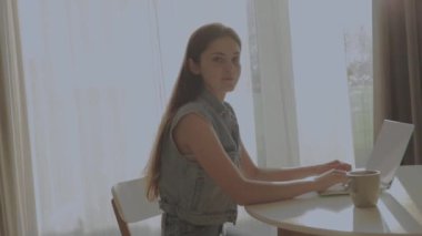 Neşeli, mutlu, pozitif ve güzel bir iş kadınının evde oturup bilgisayarını kullanması video konuşması ve mutfakta el sallaması..