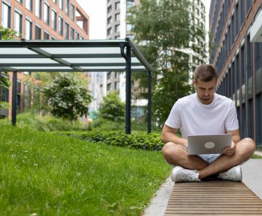 İnternette oturuyor. Ciddi bir öğrenci bankta oturuyor ve dizüstü bilgisayara bakıyor. Kulaklıkla konuşuyor.
