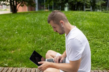 İnternette oturuyor. Ciddi bir öğrenci bankta oturuyor ve dizüstü bilgisayara bakıyor. Kulaklıkla konuşuyor.