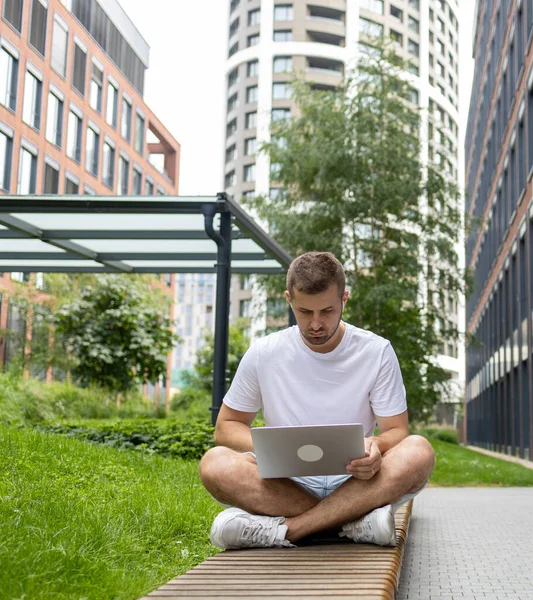 stock image Sitting on the Internet. A serious student is sitting on a bench and looking at a laptop. Speaks through headphones