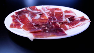 image of a white plate with serrano ham on a black background