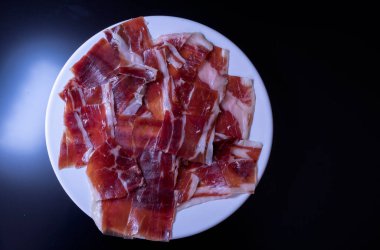 image of a white plate with serrano ham on a black background