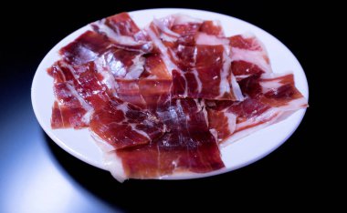 image of a white plate with serrano ham on a black background