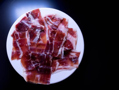 image of a white plate with serrano ham on a black background