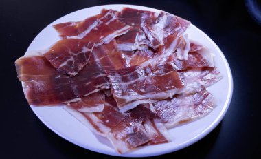 image of a white plate with serrano ham on a black background