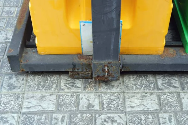 A Yellow and black recycle bins on the ground with black steel frame.