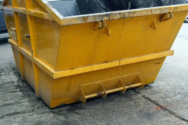 A metal yellow trash can on the street beside the market