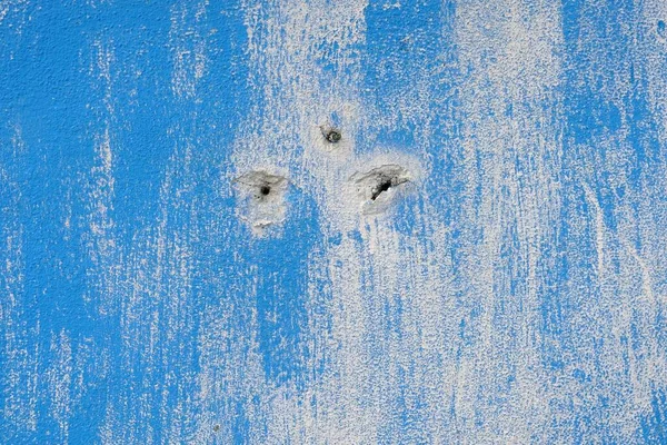 A blue painted wall with holes and peeling paint, abstract background and texture