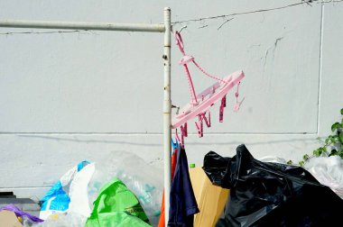 Pembe bir elbise askısı, çimento çitinin yanında da bir çöp yığını var..