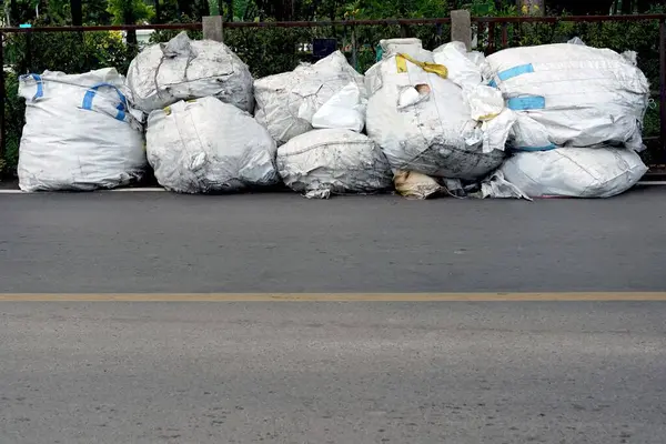 A big white pile of garbage bags on the road wait for a garbage collector.