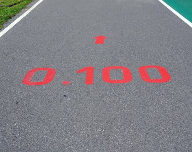 Parklardaki caddenin yüzeyinde 0.100 km işaretli kırmızı bir tabela.