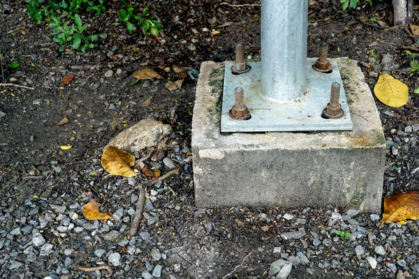 Close-up of a metal pillar installed beside a street on a cement stand in the park.