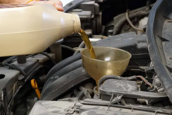 Car mechanic pouring oil into a motor oil canister in a car repair shop.