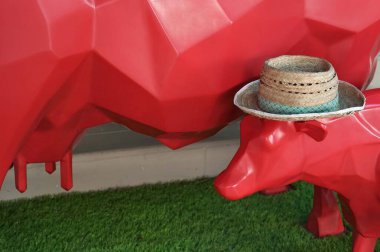 Yeşil çimen arka planında hasır şapkası olan bebek bir kırmızı inek modeli. Aşk konsepti.