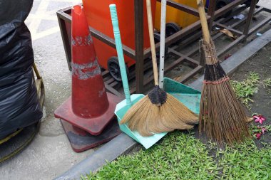 Otoparkın çimento zemininde plastik çöp kutusuyla süpürge ve temizlik malzemeleri.