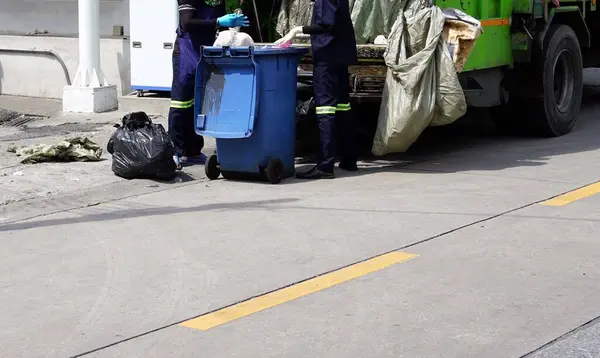 stock image A cleaner is cleaning with a green garbage truck.