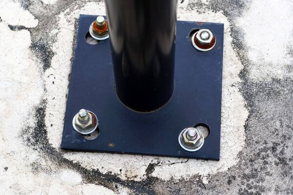 Черный столб с винтами на цементе и нижняя его часть черная.