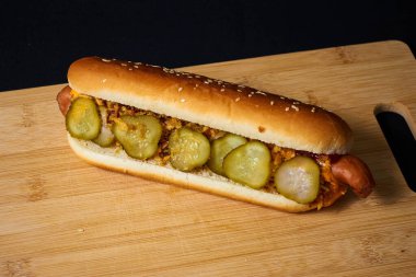 Izgara şeritli, hardallı, ketçaplı, salatalık turşulu ve soğanlı iştah açıcı sosis. Sos damlaları görünür..