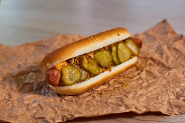 Izgara şeritli, hardallı, ketçaplı, salatalık turşulu ve soğanlı iştah açıcı sosis. Sos damlaları görünür..