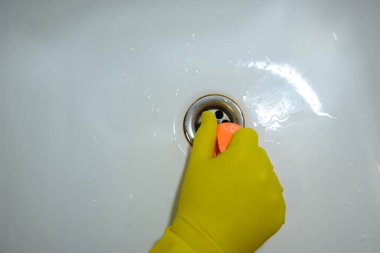 Sarı eldivenli temiz lavabo ve lağıma yakın turuncu sünger..