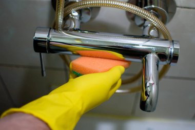 Banyoda yeşil süngerli sarı eldiven temizleme musluğu..