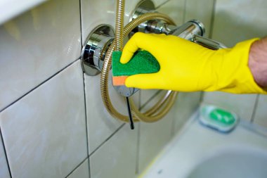 Banyoda yeşil süngerli sarı eldiven temizleme musluğu..