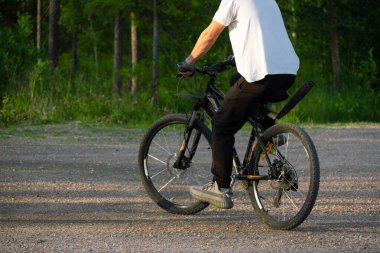 Yeşil bir parkın yanında bisiklet süren bir adam var..