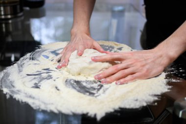 Evde pişirmek için un kaplı masaya yumuşak hamur yoğurur..