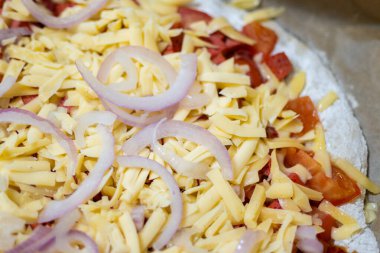 Fırına girmeden önce pizzanın üzerinde rendelenmiş peynir ve soğan halkaları..