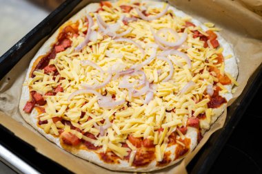 Fırına girmeden önce pizzanın üzerinde rendelenmiş peynir ve soğan halkaları..