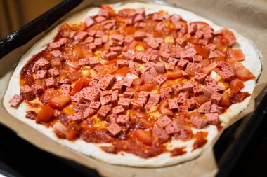 Napoli usulü ev yapımı pizza: sosis küpleri ve fırından önce taze domates.