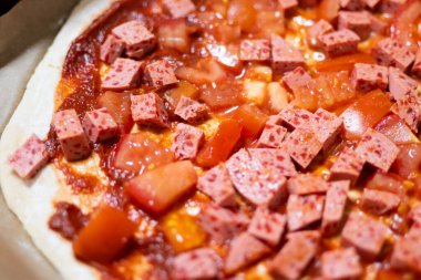 Napoli usulü ev yapımı pizza: sosis küpleri ve fırından önce taze domates.