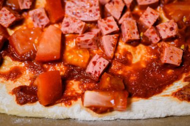 Napoli usulü ev yapımı pizza: sosis küpleri ve fırından önce taze domates.