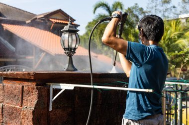 Yüksek basınçlı su püskürtme tabancası kullanan işçiler yenileme aşamasındaki konut binasında kirli duvarı yosunlarla yıkayıp temizliyor.