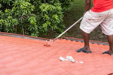 İşçi, rezidans binasında kaykayla kırmızı çatı boyuyor. Temelli ilaç yenileme uygulamasından sonra