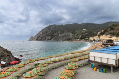 Monterosso kıyısındaki sahil boyunca uzanan renkli şemsiyeler ve sandalyeler Cinque Terre, İtalya 'daki köylerden biri olan turisti selamlıyor.
