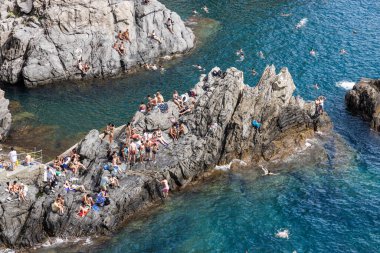 Manarola köyünün popüler deniz cephesinde güneşlenen turistler. İtalya 'nın ünlü Cinque Terre yürüyüş yolu boyunca yer alan beş köyden biridir..