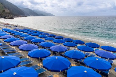 Monterosso kıyısındaki sahil boyunca uzanan renkli şemsiyeler ve sandalyeler Cinque Terre, İtalya 'daki köylerden biri olan turisti selamlıyor.