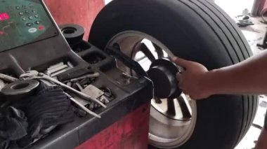 Otomobil lastiğiyle tamirhanedeki tekerlek dengeleme makinesini dengelemeye çalışan işçilere yaklaş.