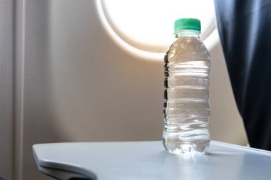 Uçak kabini penceresinin yanındaki masada, yolcuların hava yolculuğu sırasında susuz kalmaları için şişe maden suyu var.