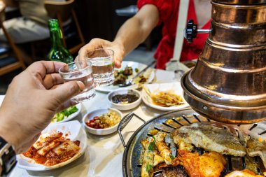İki kişi Kore barbekü restoranında soju içerken leziz ızgara etlerin tadını çıkarıyor..