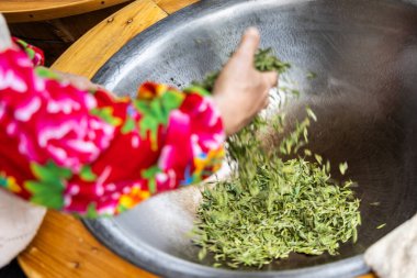 İlk işlem olarak yaprakları kurutmak için uzun çay yapraklarını tavaya atıp tutmak.