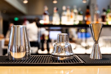 İçki karıştırıcısı ve jigger içeren parlak paslanmaz çelik çubuk seti tezgahın üzerinde bar arka planında.