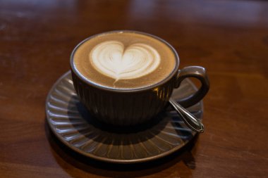 Kahverengi fincanda servis edilen güzel kalp şekilli latte ve kahverengi ahşap masa üstünde fincan fincan fincan.